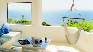 Una habitación con vistas al mar, una hamaca, un sofá con cojines, una mesita con objetos y una estatua.