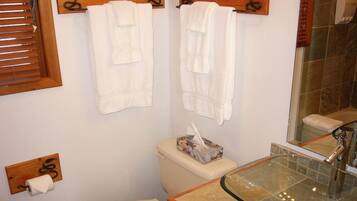 A bathroom with two white towels hanging on wooden towel racks, a glass sink with a modern faucet, and a toilet with a tissue box.