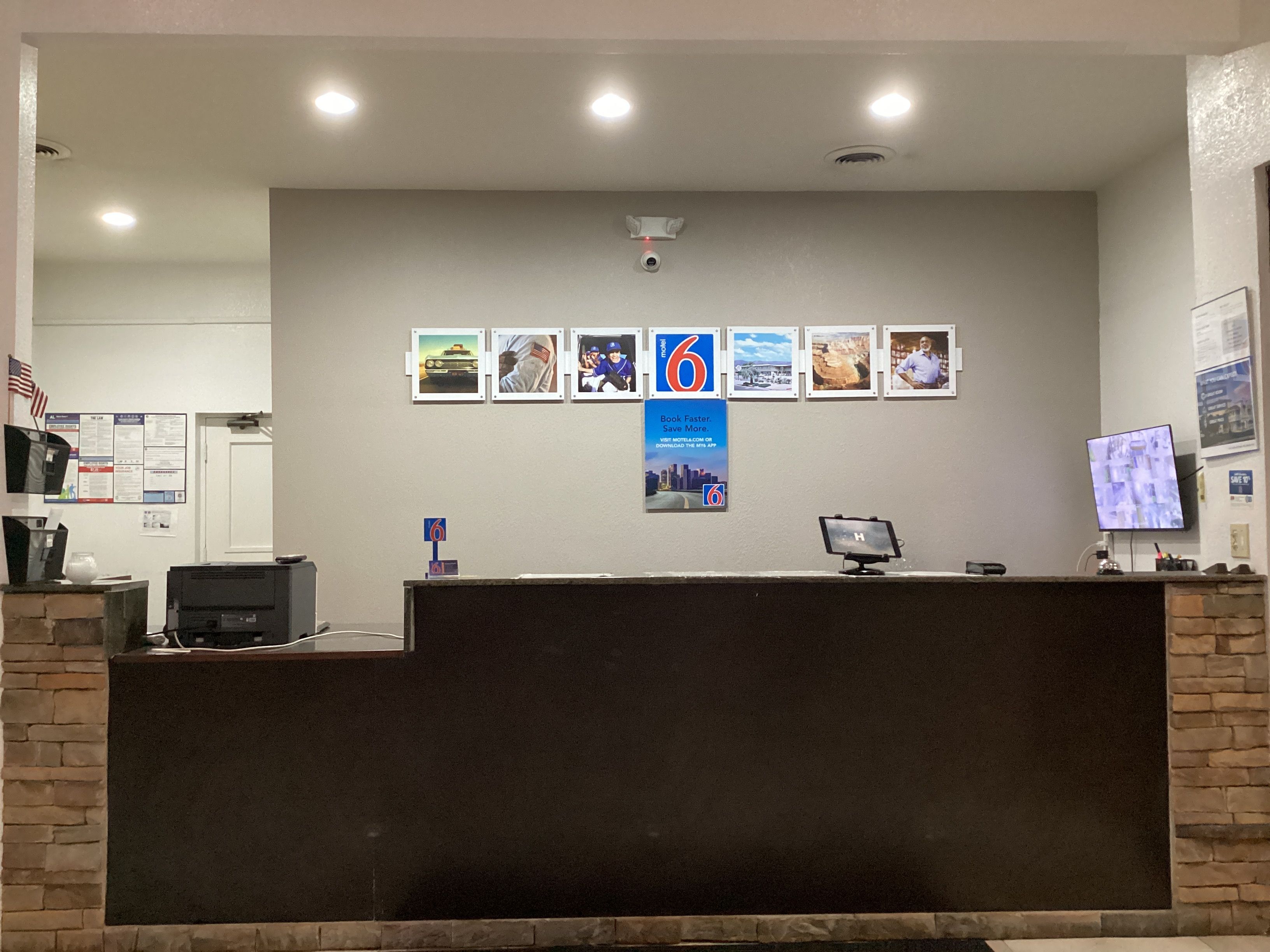 A reception desk with a computer monitor, a printer, and a wall-mounted security camera.