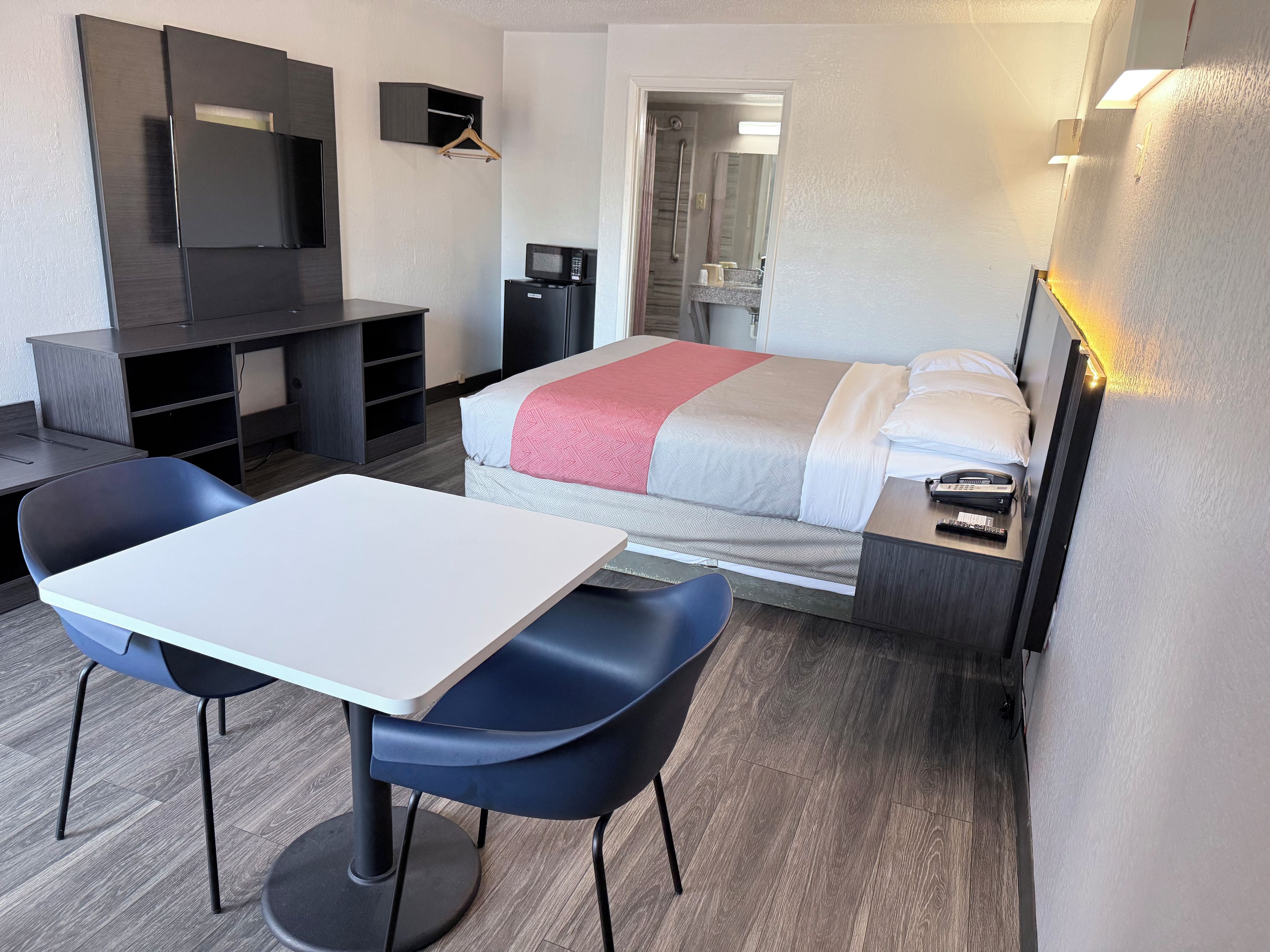 A hotel room with a bed, a desk, a chair, a TV, a microwave, and a bathroom visible through an open door.