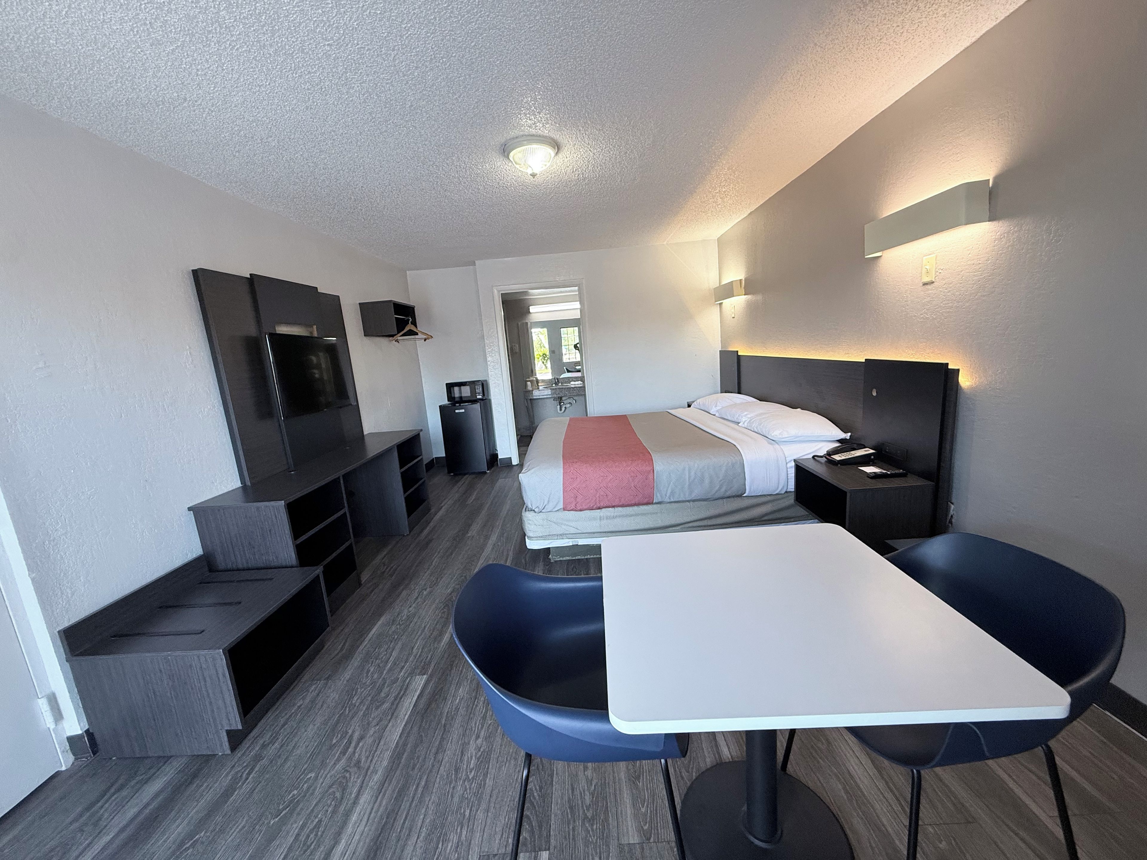 A hotel room with a bed, a desk, a chair, a TV, and a microwave.
