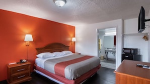 A hotel room with a bed, bedside lamps, a wooden nightstand, a desk, a television, and a microwave. - Motel 6 Montgomery, AL - Coliseum (Montgomery)