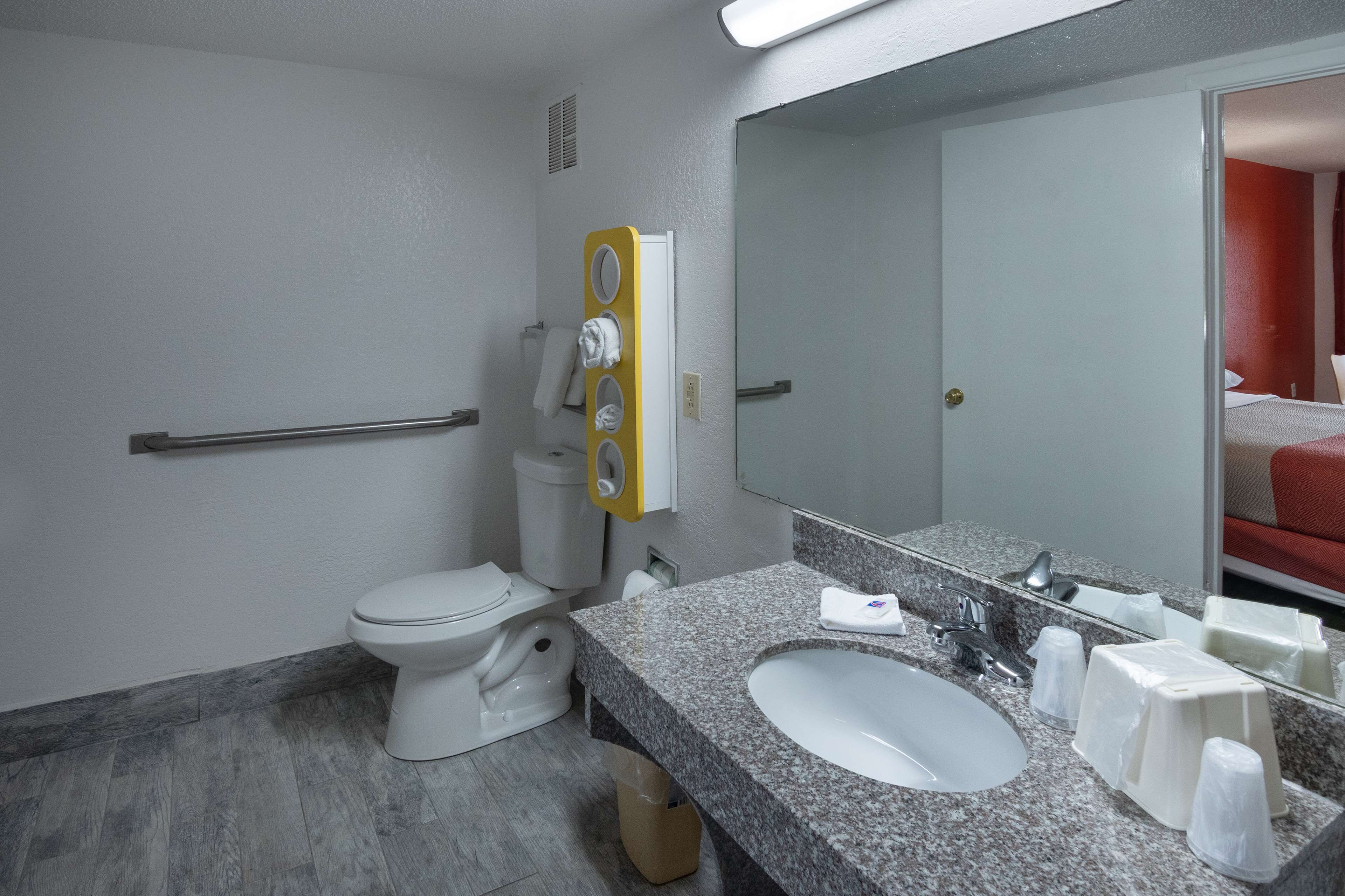 A modern bathroom with a toilet, sink, mirror, and towel dispenser.
