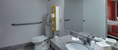 A modern bathroom with a toilet, sink, mirror, and towel dispenser.