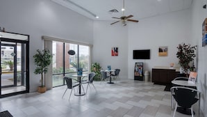 A modern reception area with a ceiling fan, large windows, and a mix of seating arrangements including tables and chairs. - Motel 6 Montgomery, AL - Coliseum (Montgomery)