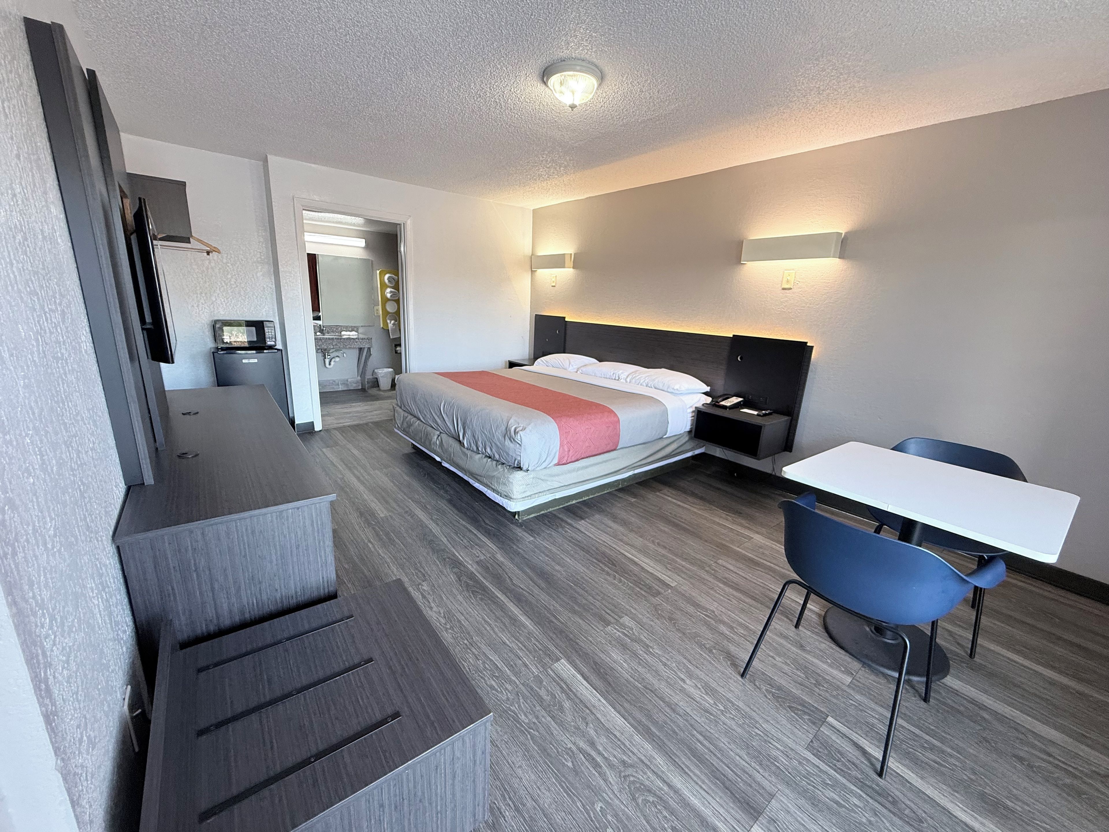 A hotel room with a bed, bedside table, desk, chair, and a view of the bathroom.