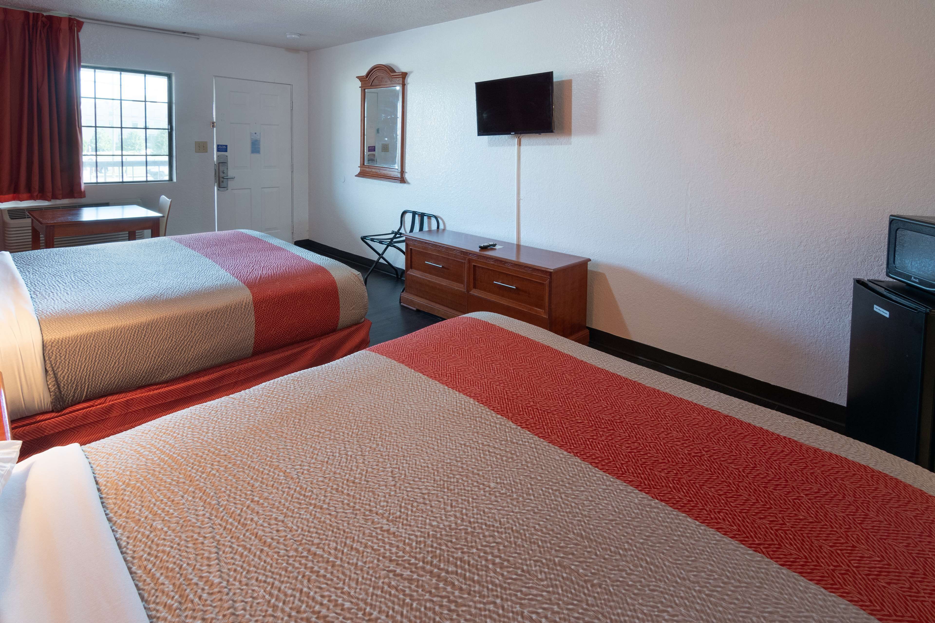 A hotel room with two beds, a desk, a chair, a dresser, and a TV.