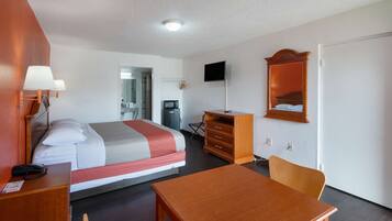 A hotel room with a bed, bedside table, lamp, desk, chair, dresser, TV, and a door.