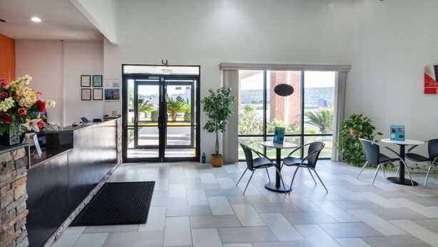A reception area with a counter, a large window, and a seating area with chairs and a table. - Motel 6 Montgomery, AL - Coliseum (Montgomery)