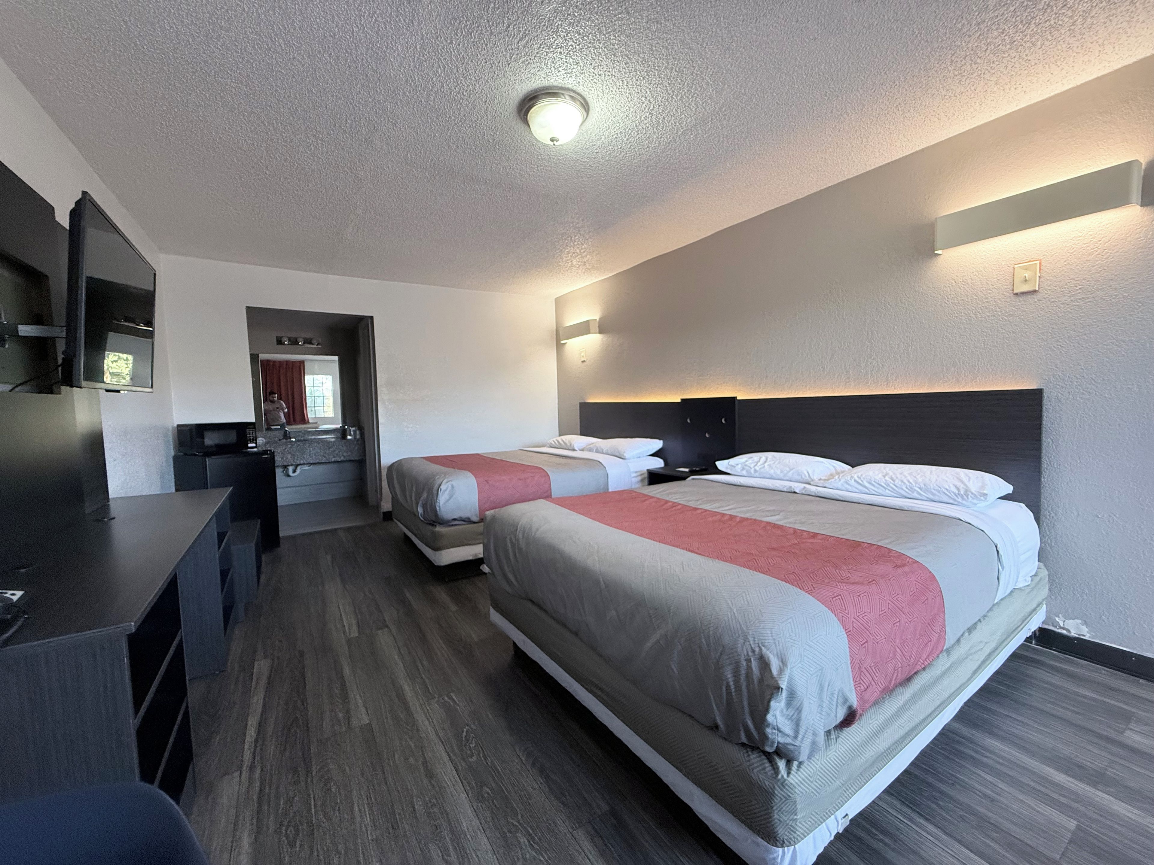 A hotel room with a bed, a desk, a mirror, and a television.
