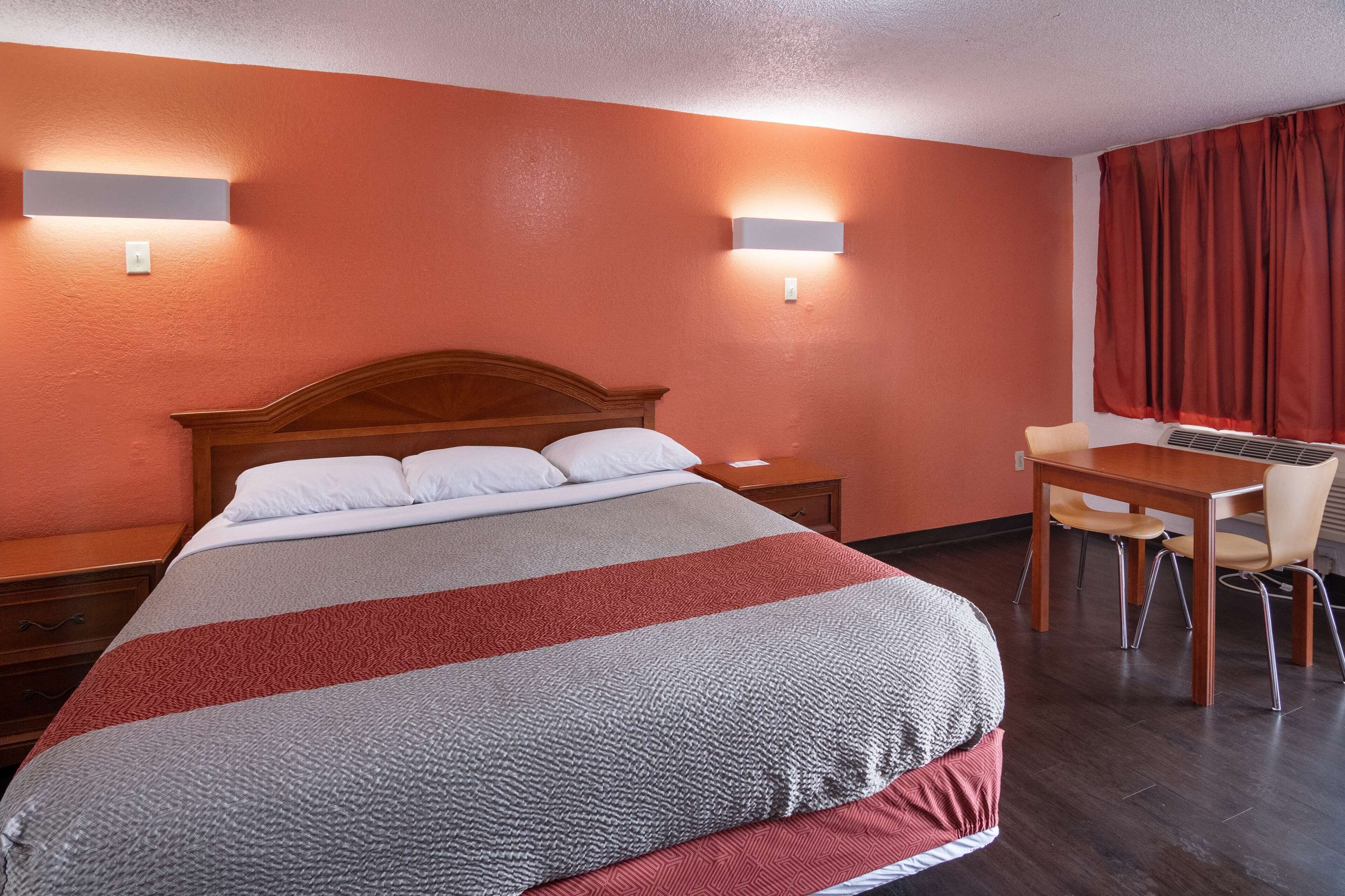 Une chambre d’hôtel avec un grand lit, une tête de lit en bois, deux tables de chevet, un bureau avec une chaise et une fenêtre avec des rideaux.