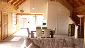 A spacious loft-style room with a high ceiling, wooden beams, a dining area with a table and chairs, and a cozy seating area with a sofa. - Charles Reuben Estate (Tea Tree)