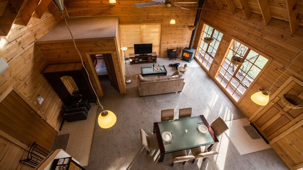 A spacious wooden cabin with a dining area, a living room with a fireplace, and large windows allowing natural light. - Charles Reuben Estate (Tea Tree)