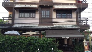 A two-story building with a restaurant named "Teeraya" on the ground floor. There are several scooters parked in front, and a hedge is visible behind the building. - Teeraya Boutique Guesthouse - Hostel (Chiang Mai)