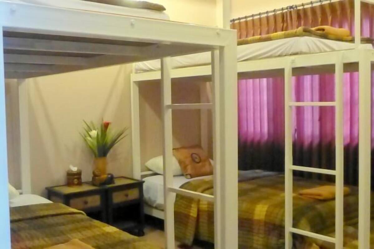 A dormitory room with bunk beds, a bedside table with a lamp, and a window with curtains.