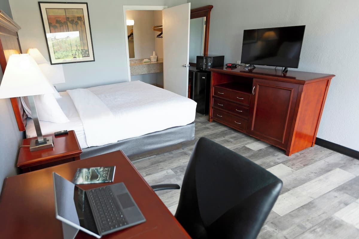 A hotel room with a bed, desk, chair, TV, and a bathroom visible through an open door.