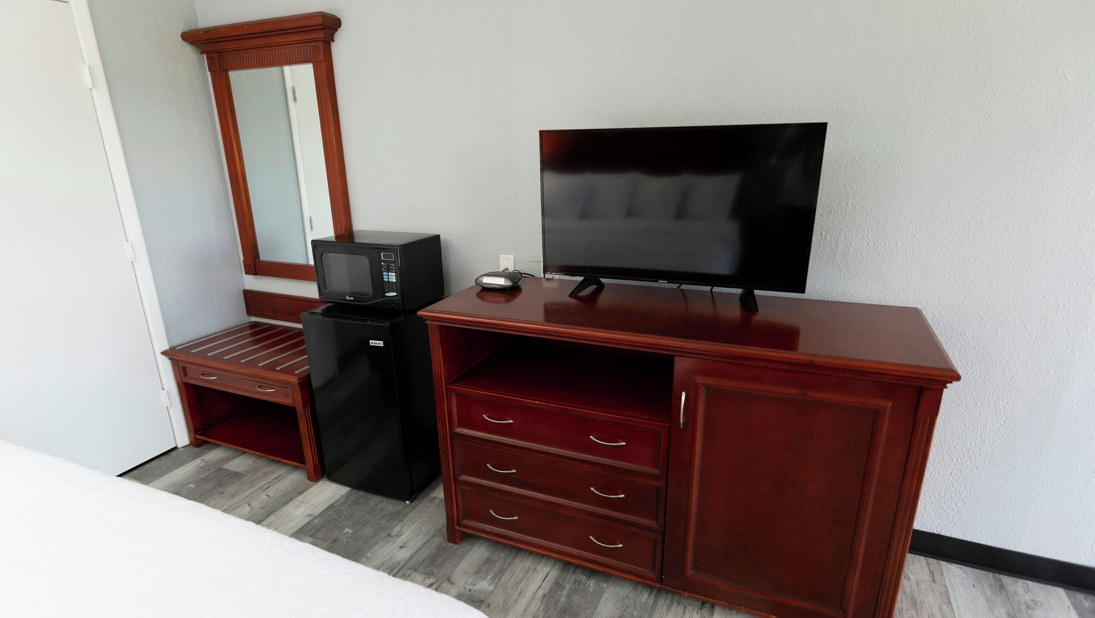 Una habitación con un escritorio de madera, televisor, microondas y refrigerador.