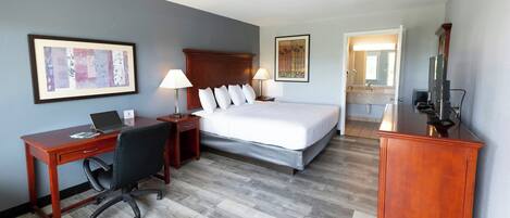 Habitación de hotel con cama, escritorio, silla, lámpara y televisión.