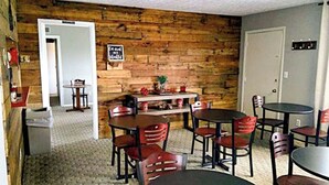 A room with a wooden wall, a door, a table with chairs, and a small shelf with items. - Sunrise Inn Williamstown (Williamstown)