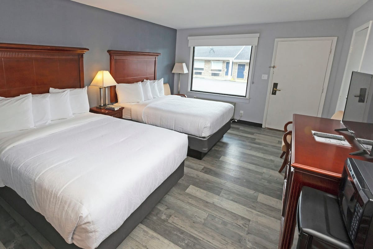 A hotel room with two beds, a desk with a computer, a TV, and a window with a view of the outside.