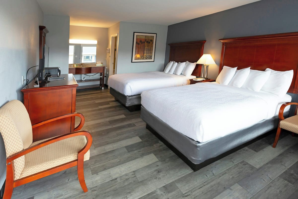 A hotel room with two beds, a desk, a chair, and a lamp.