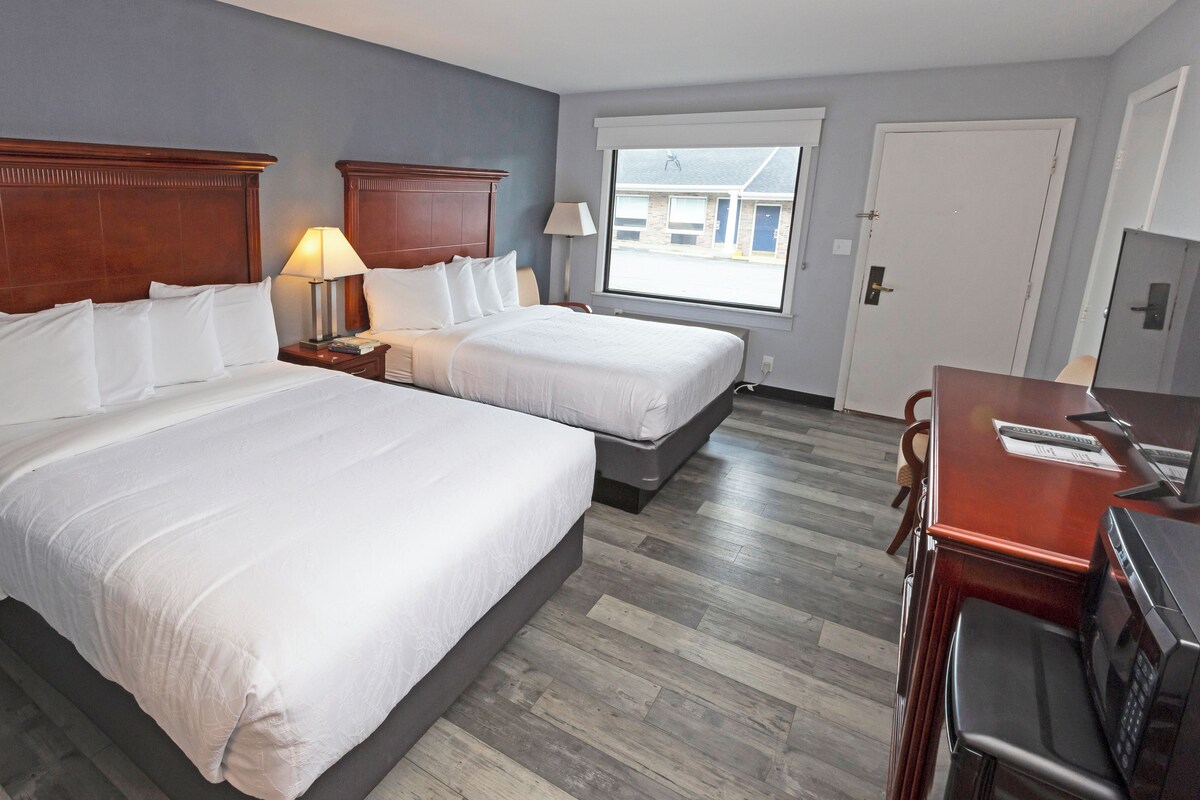 A hotel room with two beds, a desk with a computer, and a window with a view of the street.