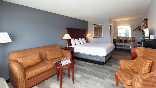 A hotel room with a bed, two sofas, a small table, a desk, a mirror, and a bathroom. - Sunrise Inn Williamstown (Williamstown)