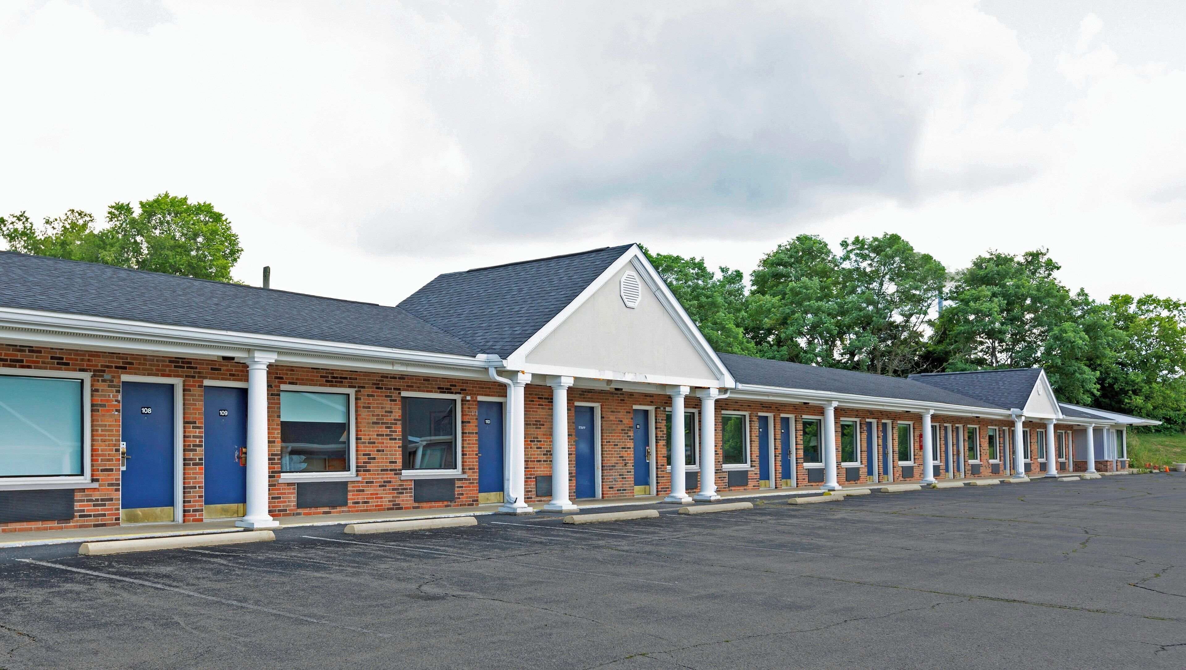 A motel with a row of rooms, each with a door and window, and a parking lot in front.