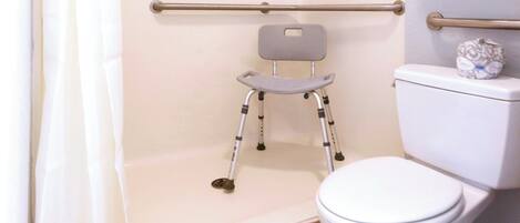 Une salle de bain équipée d’une douche accessible aux personnes en fauteuil roulant, de toilettes et d’une barre d’appui.