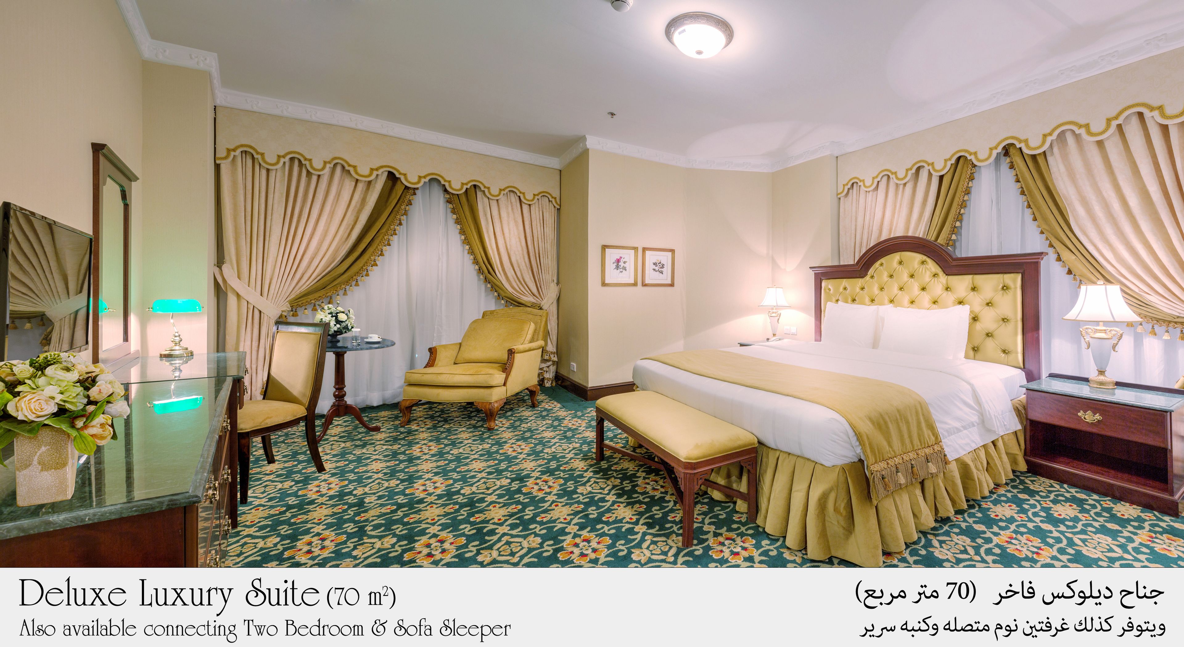 A Deluxe Luxury Suite with a Two Bedroom & Sofa Sleeper layout, featuring a floral carpet, a large bed with a gold headboard, a sitting area with a yellow armchair, and a dining table with a vase of flowers.