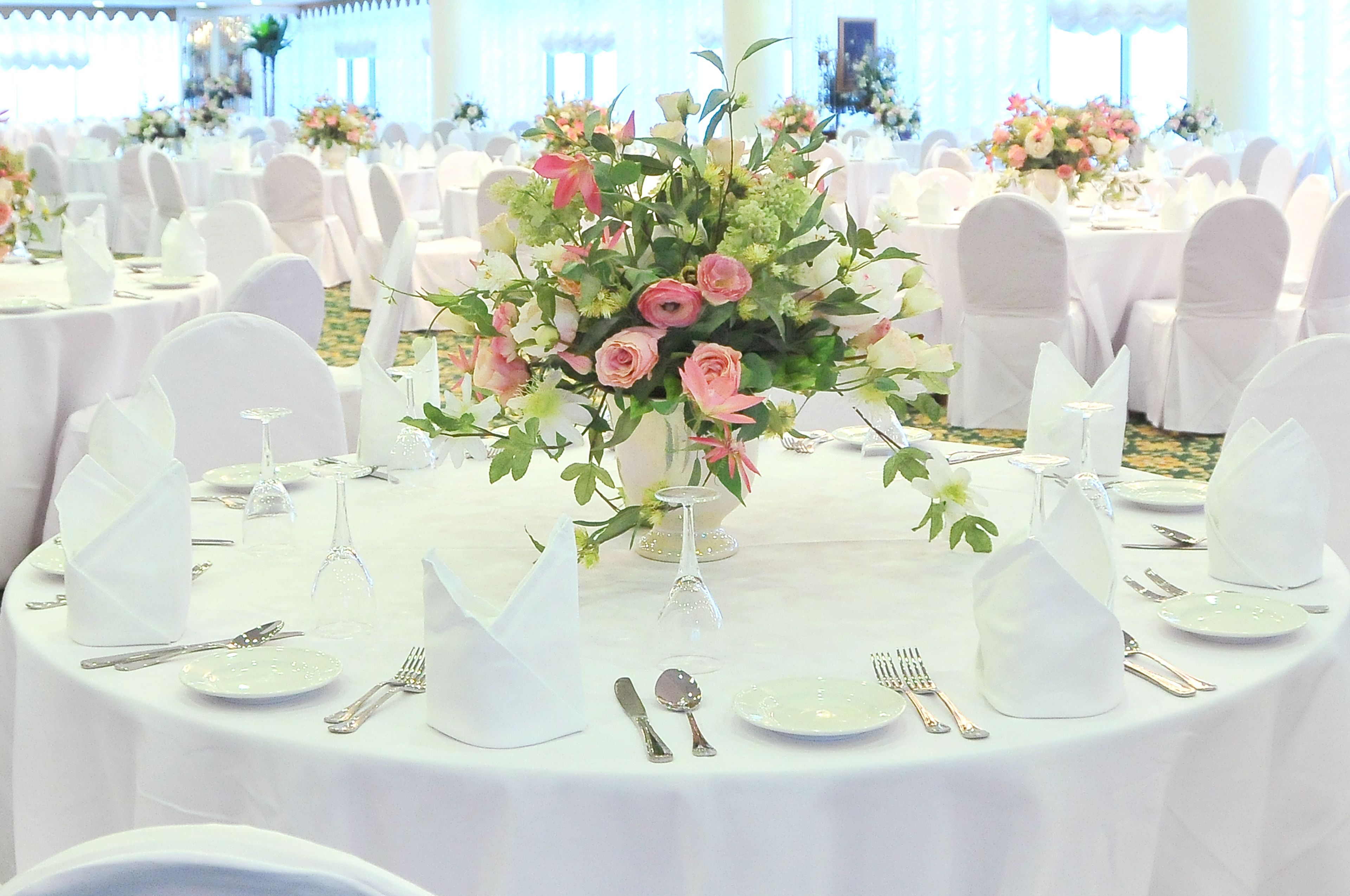 A banquet hall with round tables set for a formal event, each with white tablecloths, glassware, and floral centerpieces.