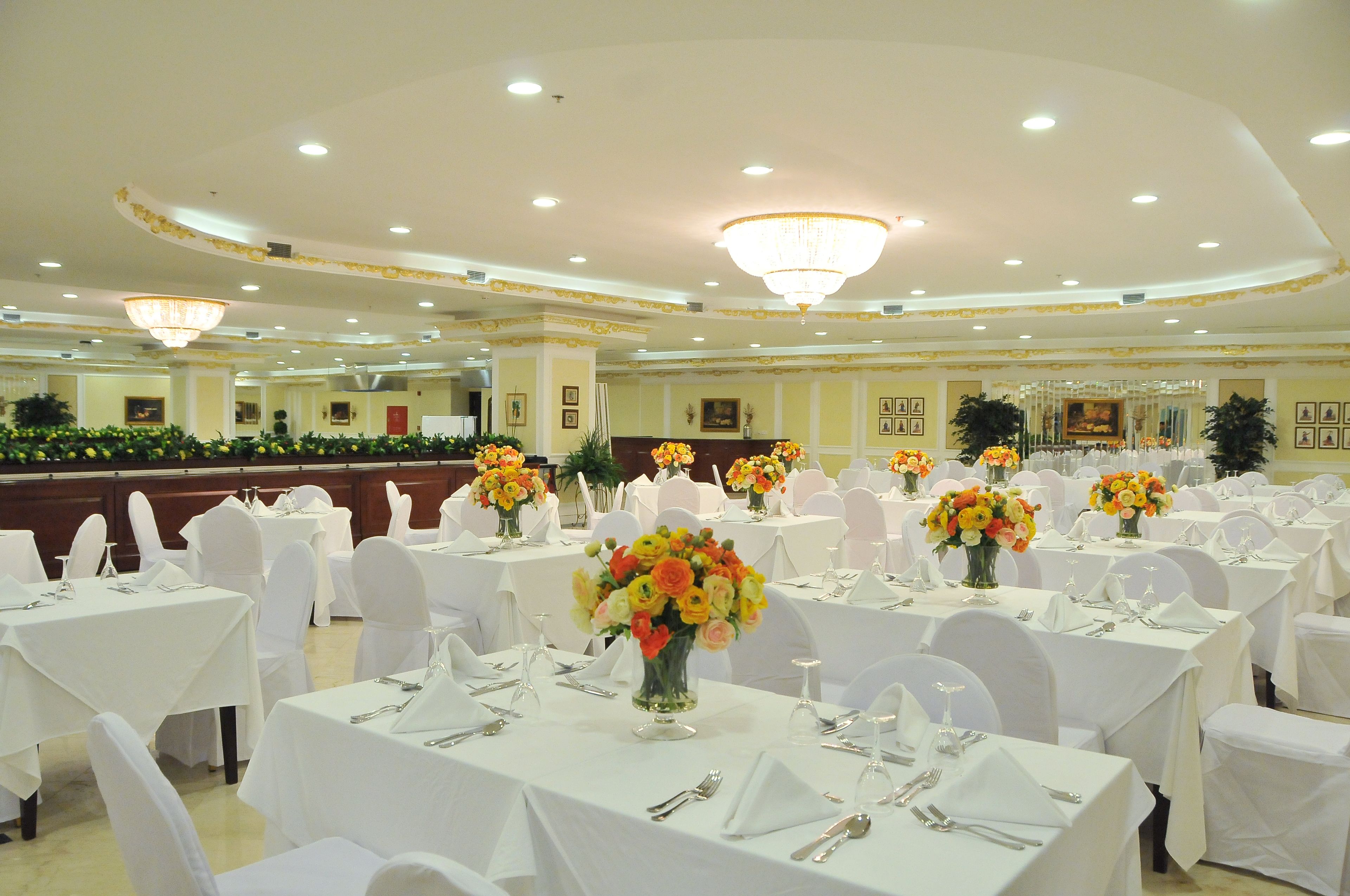 A banquet hall with round tables set for dining, each with a vase of flowers and white tablecloths.