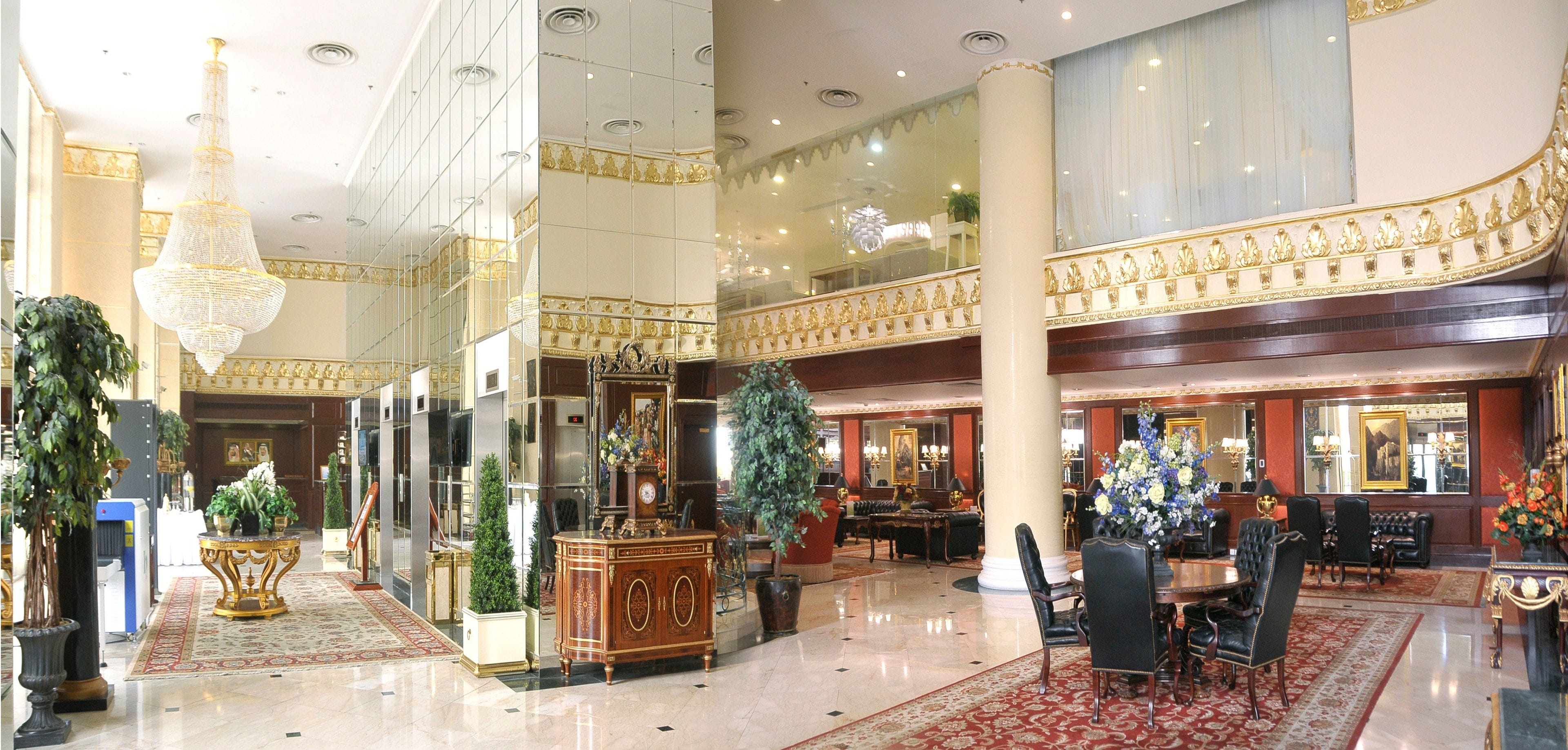 A spacious lobby with a grand chandelier, ornate columns, and a high ceiling.