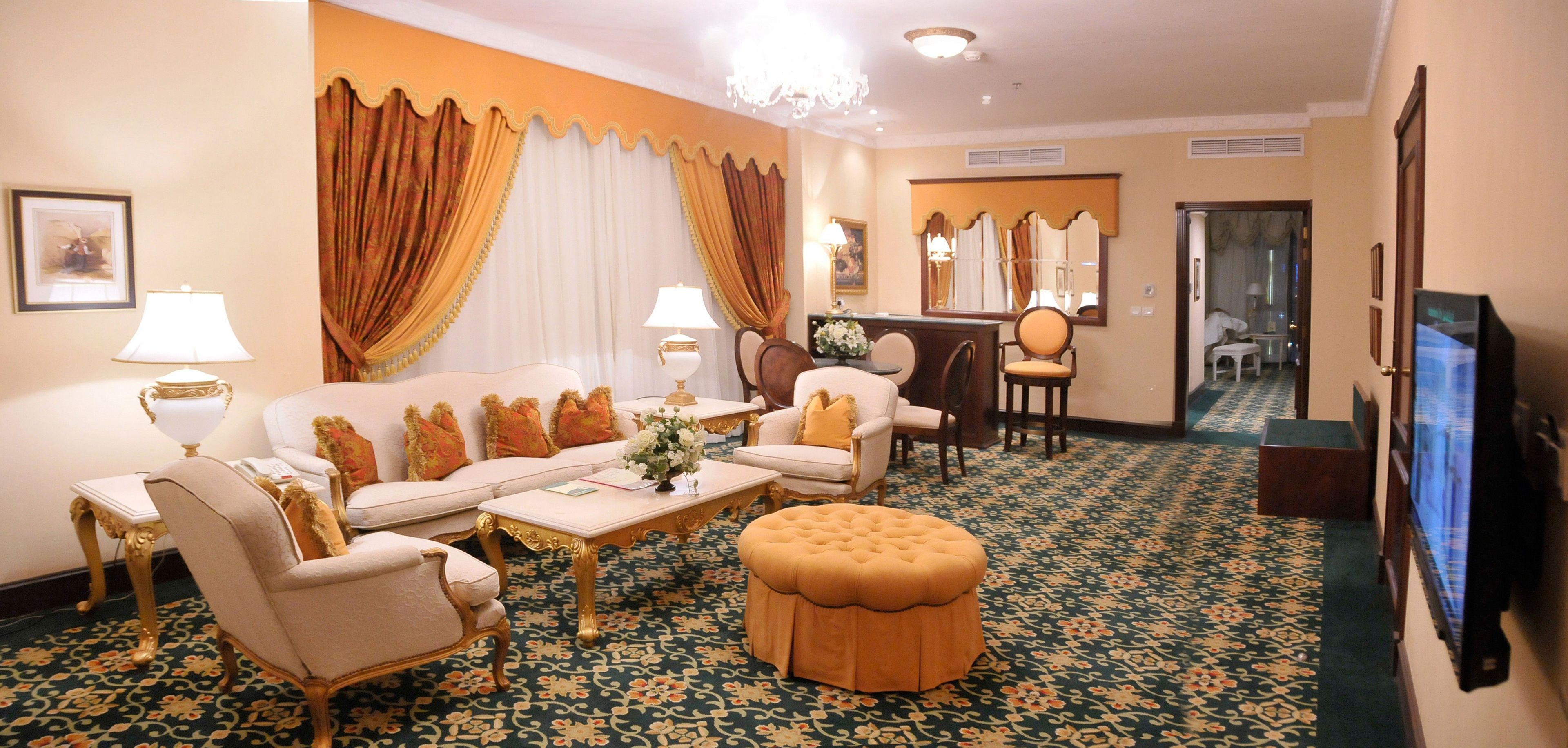 A hotel room with a sofa, armchairs, a coffee table, a TV, and a desk with a chair.