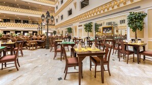 A spacious, multi-level dining area with numerous tables and chairs, ornate ceiling details, and large windows.