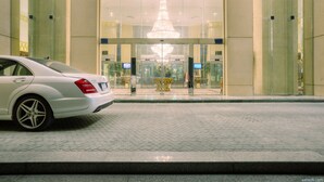 A white car parked in front of a building with a large chandelier and a glass entrance.
