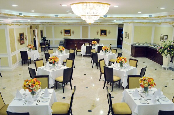 Une salle à manger élégante, avec plusieurs tables dressées pour le service, un bar central et un lustre.