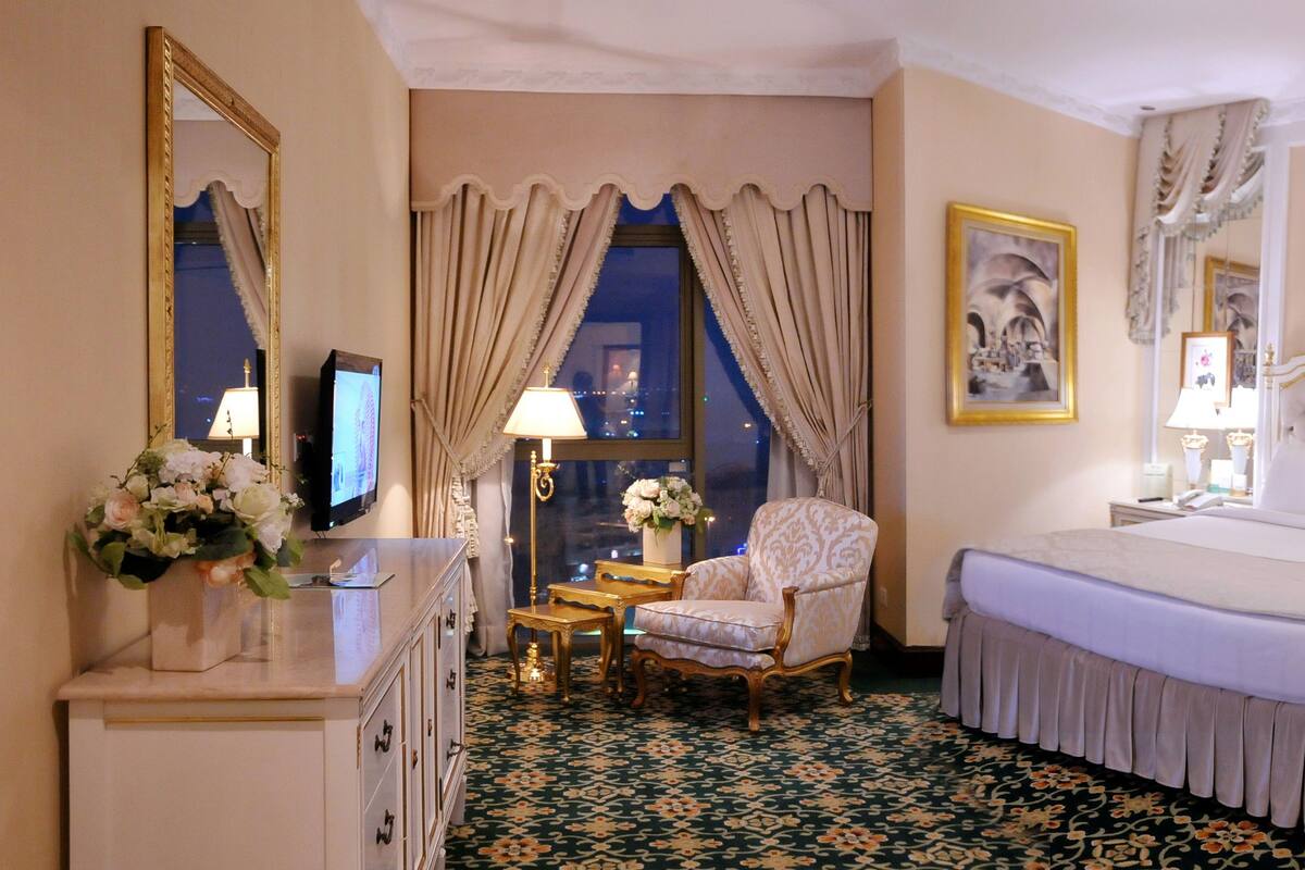 A hotel room with a large bed, a chair, a desk, and a dresser.