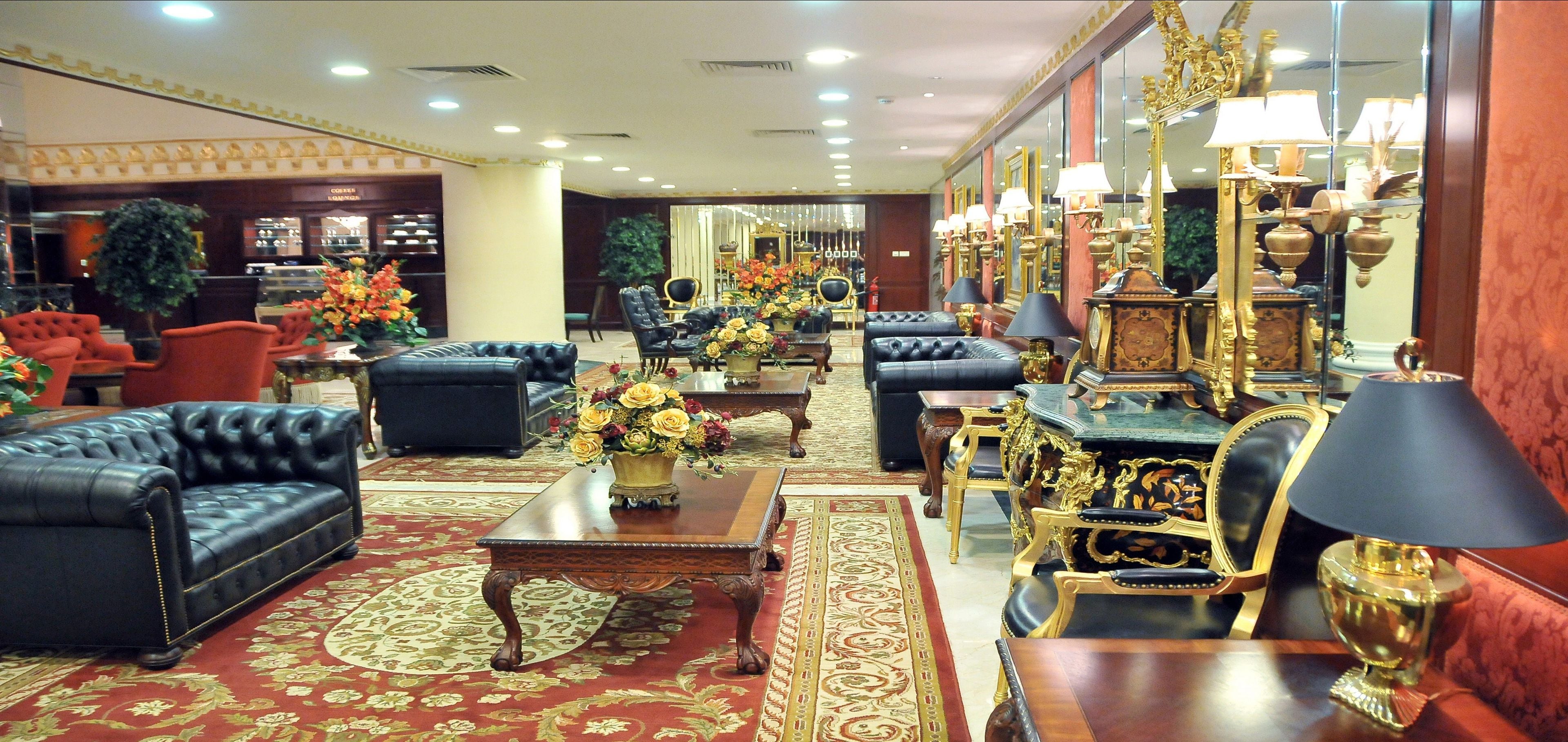 A luxurious lobby with leather sofas, ornate furniture, and a large mirror reflecting the room.