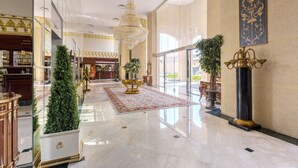 A spacious lobby with a marble floor, a large chandelier, and a decorative wall piece.