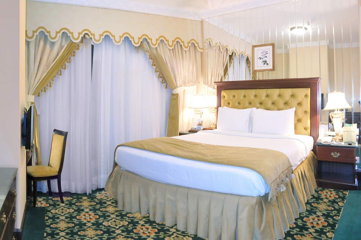 A hotel room with a large bed, a chair, a nightstand, and a dresser.