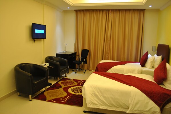 A hotel room with two beds, a desk, a chair, a TV, and a large window with curtains.