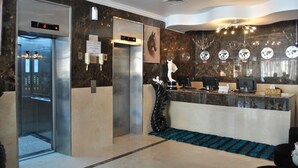 A hotel lobby with two elevators, a reception desk, and a decorative wall with clocks. - Mirage Hotel Al Aqah (Dhadnah)