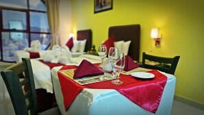 A dining area with tables set for two, featuring red napkins, wine glasses, and cutlery. - Mirage Hotel Al Aqah (Dhadnah)