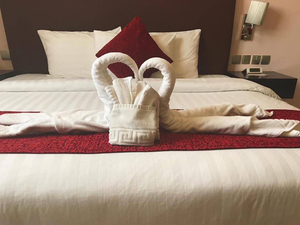 Una cama con sábanas blancas, una manta roja y una toalla doblada en forma de cisne.