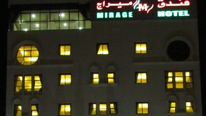 A multi-story hotel with illuminated windows and a neon sign indicating it is the Mirage Hotel. - Mirage Hotel Al Aqah (Dhadnah)