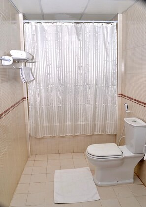 A bathroom with a toilet, a shower curtain, and a towel on the floor. - Sara Hotel Apartment (Ajman)
