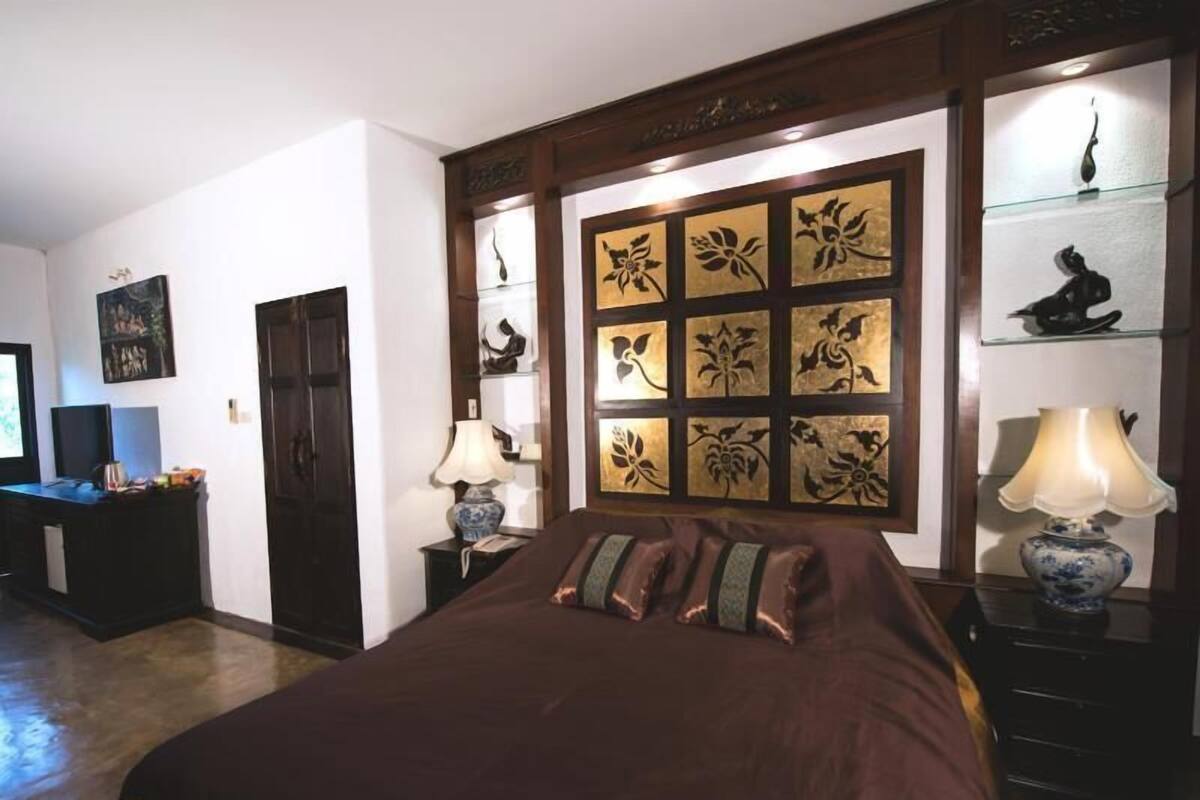 Une chambre avec un grand lit, une table de chevet avec une lampe, une commode, un bureau avec un ordinateur et un mur orné de panneaux décoratifs.
