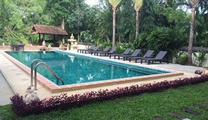 A swimming pool with lounge chairs, a small pavilion, and lush greenery.