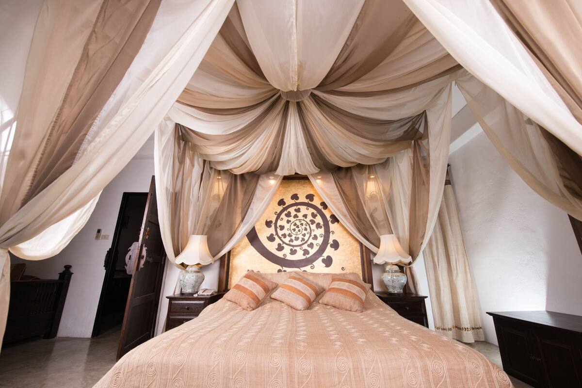 Une chambre à coucher avec un grand lit, des rideaux élégants et des œuvres d’art décoratives accrochées au mur.